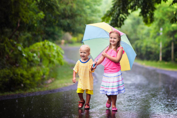 istock Kid with umbrella playing in summer rain. 1272095910