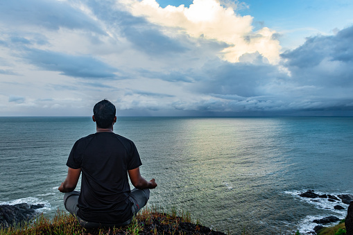 man meditating at the hilltop with amazing landscape and sea horizon at the morning image is taken at gokarna karnataka india. the view from here is pristine and mesmerizing.