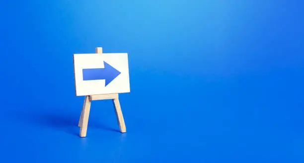 Photo of Easel with a blue right arrow. Sign of direction. Advertising of the location of a store or outlet. Minimalism. Distracting maneuver. Restriction of movement, change of course. Short road.