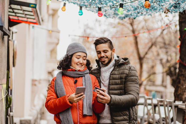 Young couple shopping online outdoors Multi-ethnic couple outdoors using credit card and mobile phone to pay holiday shopping stock pictures, royalty-free photos & images