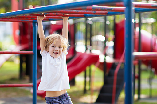 Child playing on outdoor playground in rain. Kids play on school or kindergarten yard. Active kid on colorful monkey bars. Healthy summer activity for children. Little boy climbing.