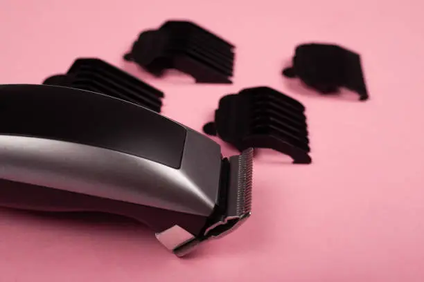 hair clipper with nozzles on a pink background close-up, hairdressing tools.
