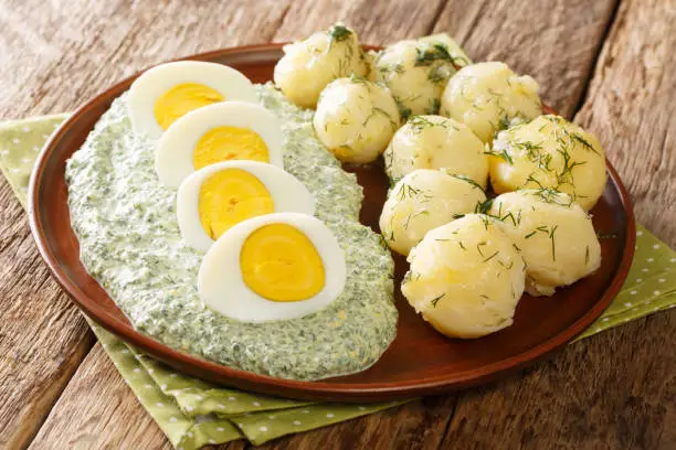 German style dish of potatoes, boiled eggs and green sauce close-up in a plate on the table. horizontal
