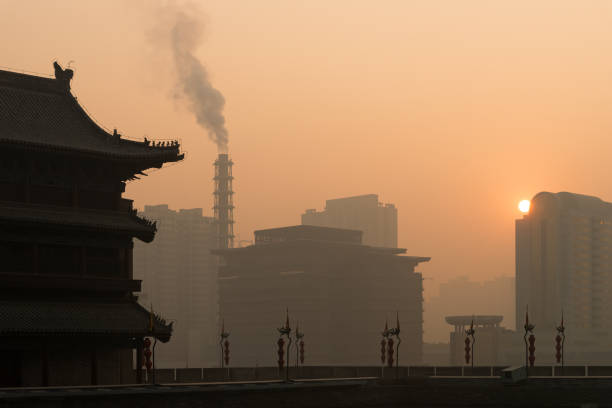 Traditional Chinese building and 14th century city wall in Xian, China with smokestack and modern buildings in the background at sunset