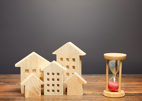 Wooden figures of houses and sand hourglass. Mortgage and loan concept. Temporary rental housing and residence permit. Time to pay taxes and bills. Real Estate Agent services for a quick search for options.