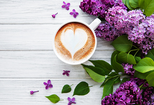 Lilac and cup of coffee  in flat style on white wooden background. Beautiful spring. Overhead view. Flat lay, top. Summer season. Natural spring style.