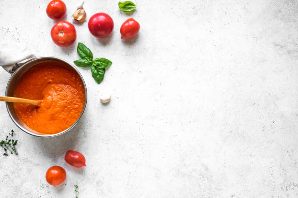 Tomato sauce or soup Homemade tomato sauce in cooking pan and ingredients on white table, top view, copy space. Making organic italian tomato sauce or soup. marinara stock pictures, royalty-free photos & images