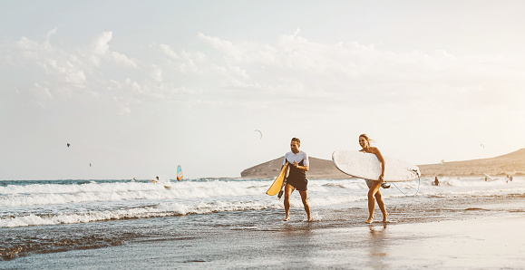 Surfer couple running long sea shore ready to surf on high waves - Sporty friends having fun during surfing day in ocean - Extreme sport health lifestyle people concept