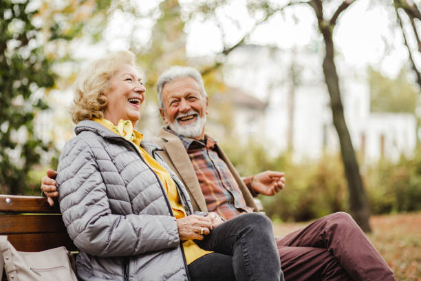 счастливая старшая пара сидит на скамейке в парке - cheerful retirement senior women vitality стоковые фото и изображения