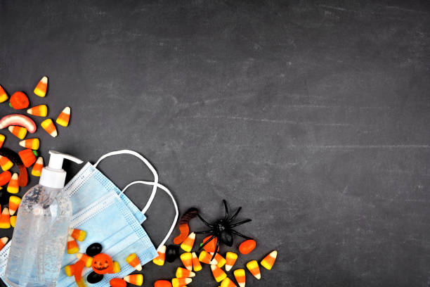 Halloween during coronavirus corner border with candy, face mask and hand sanitizer over a black background
