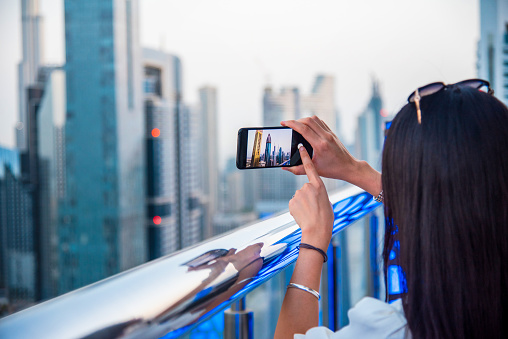 Woman taking a photo of Dubai downtown skyline in the United Arab Emirates with a smart phone