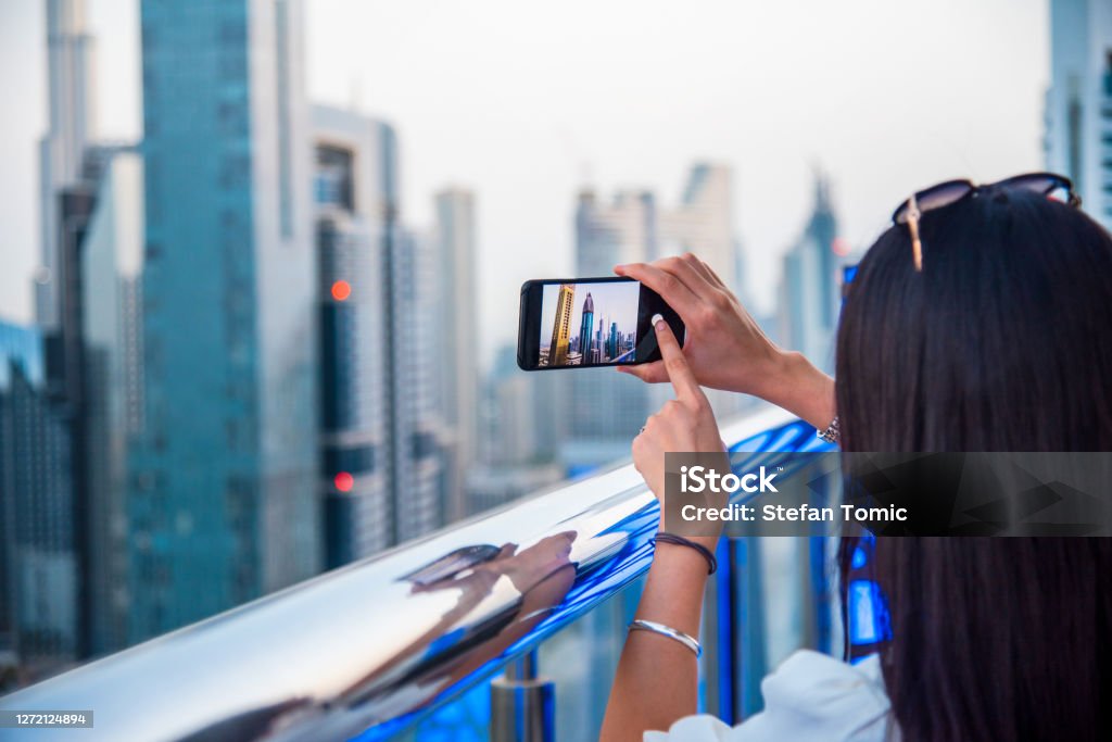 Woman taking a photo of Dubai downtown skyline in the UAE with a smart phone Woman taking a photo of Dubai downtown skyline in the United Arab Emirates with a smart phone Dubai Stock Photo