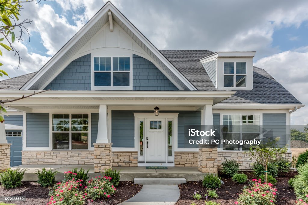 Home with blue siding and stone façade on base of home Lots of shrubs and mulch in beautifully landscaped yard House Stock Photo