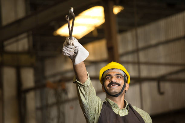 Confident industrial worker in protective workwear holding wrench at factory