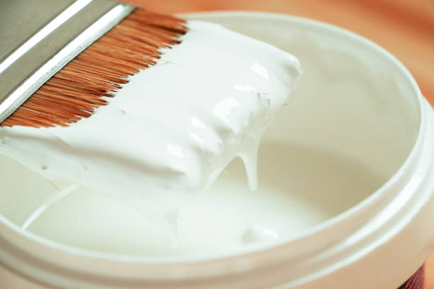 White paint is flowing from the brush into the can. The brush was taken out of the can and white paint drips off the brush. Close-up. The concept of repair and do it yourself. color buckets stock pictures, royalty-free photos & images