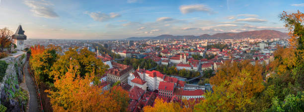 paesaggio urbano di graz e torre dell'orologio, famosa attrazione turistica sulla collina di shlossberg, graz, regione della stiria, austria, in autunno. vista panoramica. - autumn clock roof colors foto e immagini stock