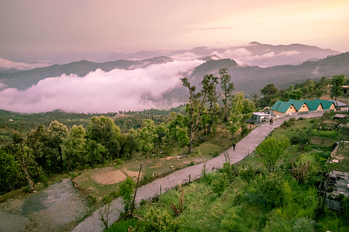 Aerial view of a road leading to a resort with misty HImalayan mountains in the village of Chaukori in Uttarakhand, India.