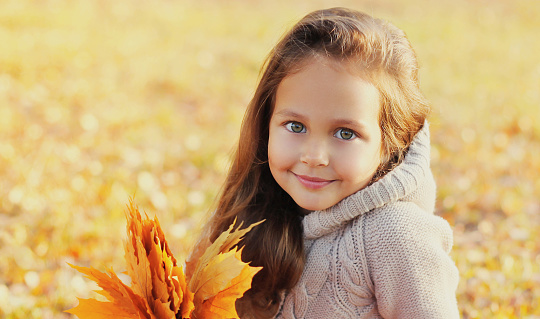 Close up portrait of happy smiling child with yellow maple leaves in autumn park