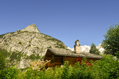 Exterior of a typical mountain house with an Alpiine peak in the background in summer, Courmayeur, Aosta Valley, Italy