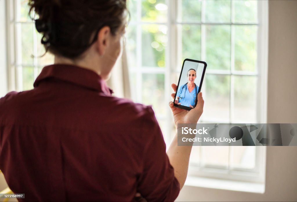 Woman consulting her doctor using an app on her smart phone Young woman using a smart phone app to consult with a doctor in real time while standing at home Telemedicine Stock Photo