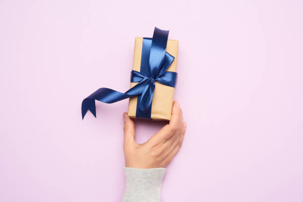 istock female hand hold a gift paper box on a purple background 1272159064