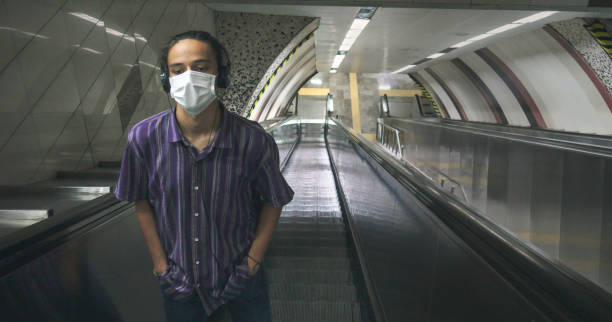 Isolated masked smart looking teenager listening to music standing on escalator stock photo