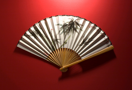 Asian folding hand fan, on red background.