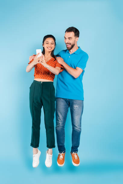 istock excited man touching shoulders of asian girlfriend using smartphone while levitating on blue 1272165268