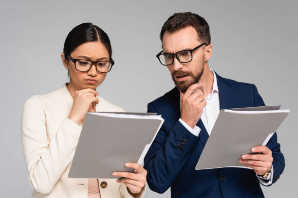 istock thoughtful interracial business partners in eyeglasses touching chins while looking at documents isolated on grey 1272165314