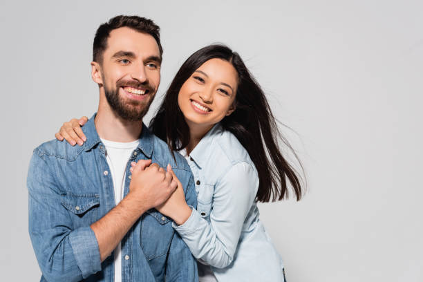 istock young asian woman looking at camera while holding hands with boyfriend isolated on grey 1272165362