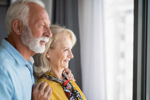 istock Happy senior couple looking through window at home. 1272173434