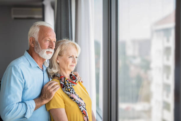 istock Senior couple looking through window at home. 1272174417
