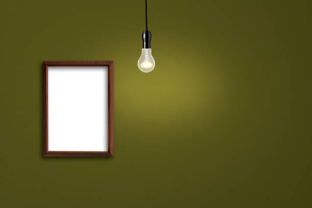 istock Wooden blank picture frame on the wall, and hanging a glowing light bulb. 1272181788