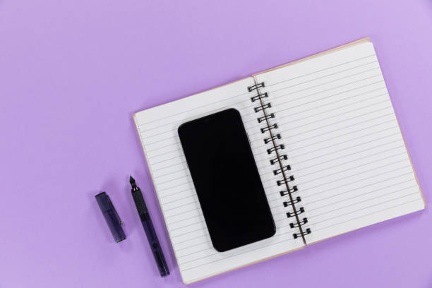 istock View of a black smartphone, a notebook and a black pen on plain purple background 1272187372