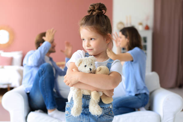 istock Young parents sitting opposite each other on couch swearing loudly and gesturing with hands while little defenseless daughter upset looking at camera. 1272197836