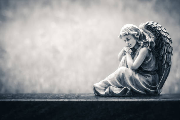 Angel figure sitting on an old headstone in a cemetery. Vintage, retro monochrome image with copy space. Halloween, all saints background concept - fotografia de stock