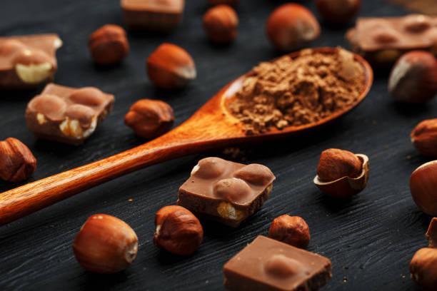 istock Chocolate with hazelnuts and a wooden spoon with cocoa on a dark background, surrounded by nuts in the shell and peeled. 1272207522