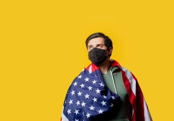 istock guy in facemask hold USA flag on yellow background 1272208420