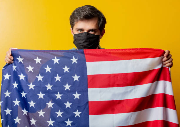 istock guy in facemask hold USA flag on yellow background 1272208422