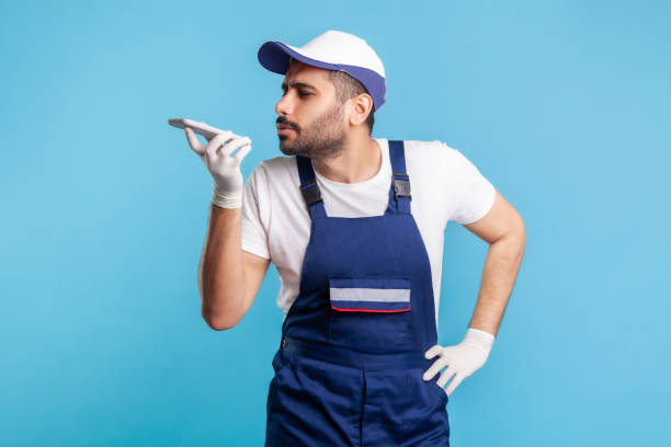 istock Virtual assistant. Handyman in overalls and gloves talking to phone recording message, using digital voice 1272208676