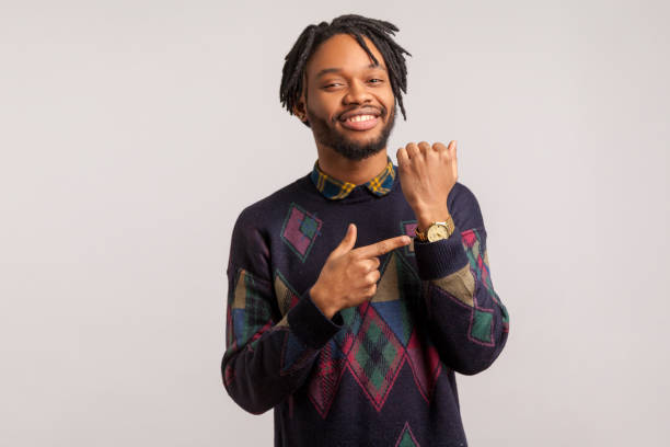 istock Cheerful successful african man with dreadlocks in stylish sweatshirt pointing finger on his watch with toothy smile on face, happiness, time management 1272208811