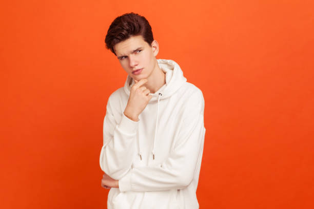 thoughtful young man in casual sweater with hood holding his chin, thinking over plans, looking for solution - pensive question mark teenager adversity imagens e fotografias de stock