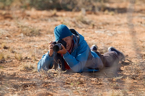 A wildlife photographer lying flat on her stomach photographing wildlife