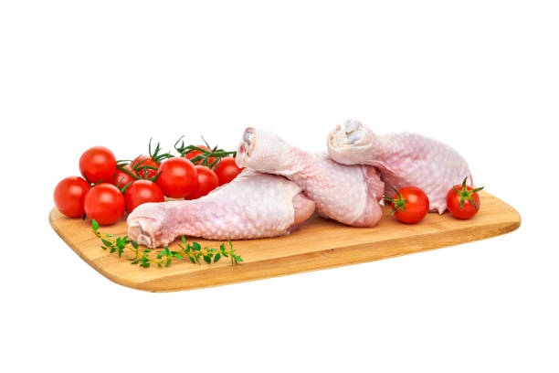 istock Three fresh raw chicken drumsticks on a wooden chopping Board with vegetables and herbs, on a white background. 1272217224