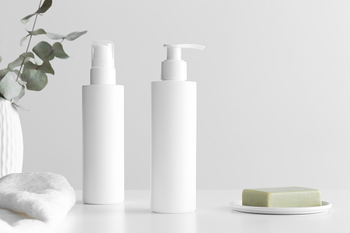 Set of white cosmetic bottles mockup with a towel, natural soap and eucalyptus branches on a white table.