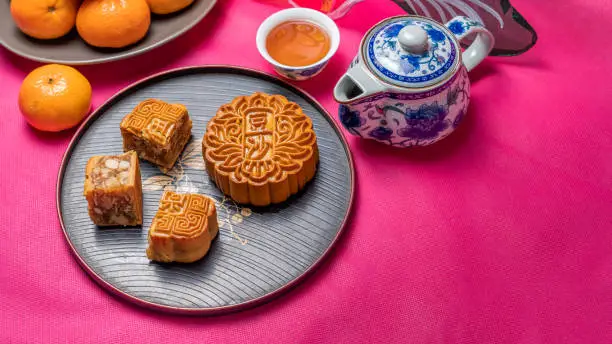 High angle studio shot of mooncake and tea set on bright pink background. The table is decorated with oranges and lantern.