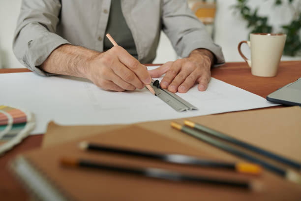 istock Close-up of unrecognizable engineer sitting at desk and using ruler while working on house plan 1272232777