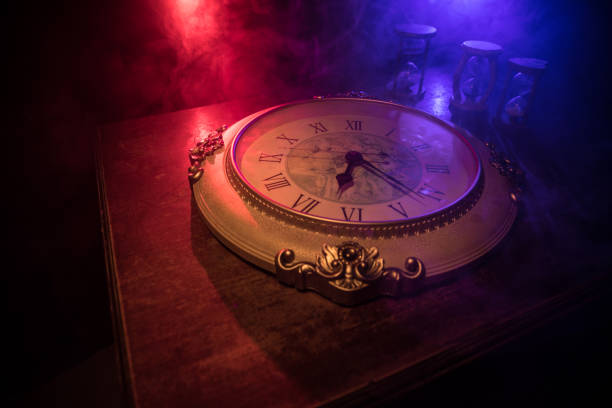 istock Time concept. Big vintage round clock on wooden table with abstract light. 1272232795