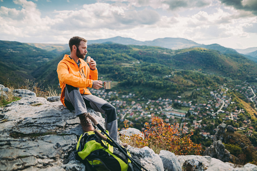 Young man in the mountain sitting on the rocks and eating breakfast with cup of hot tea