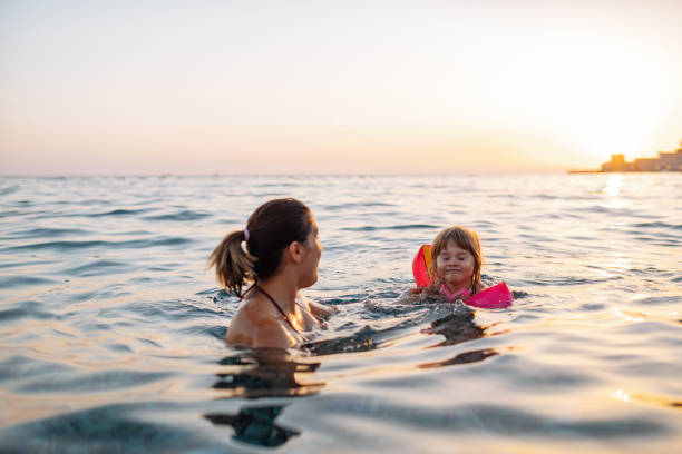 bambina di tre anni che nuota in mare imparando a nuotare, indossando ali d'acqua - women courage water floating on water foto e immagini stock